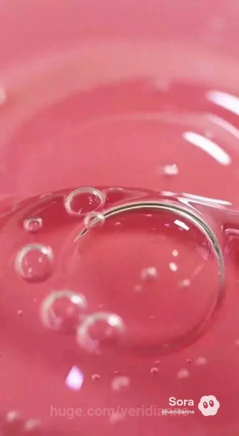 Close-up of vibrant pink viscous liquid with many small and large bubbles moving and popping.