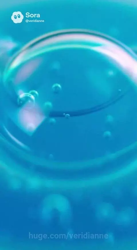 Close-up of a viscous blue liquid with numerous rising bubbles, showing iridescent pink and green reflections.