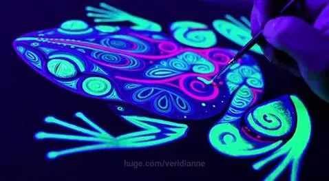 Close-up of a frog painting with neon green, pink, and blue fluorescent paints under black light.