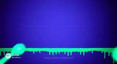 Neon green and blue paint splatters and drips on a dark surface under blacklight.