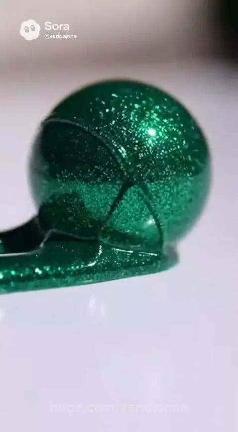 Close-up of a shimmering emerald green liquid forming a sphere with a metallic, glittery texture on a white surface.