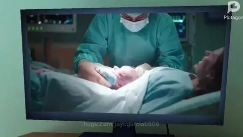 Two animated characters on a couch, one bald, discussing baldness. TV shows a hospital birth scene.