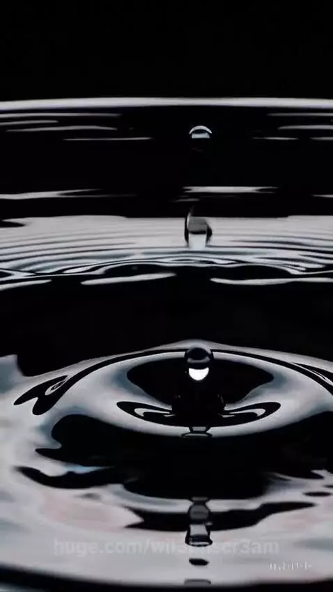 Close-up of a water drop falling into dark liquid, creating intricate ripples in slow motion.
