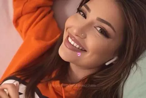 Animated character with long brown hair and nose piercing, wearing an orange hoodie, dancing with colorful confetti.