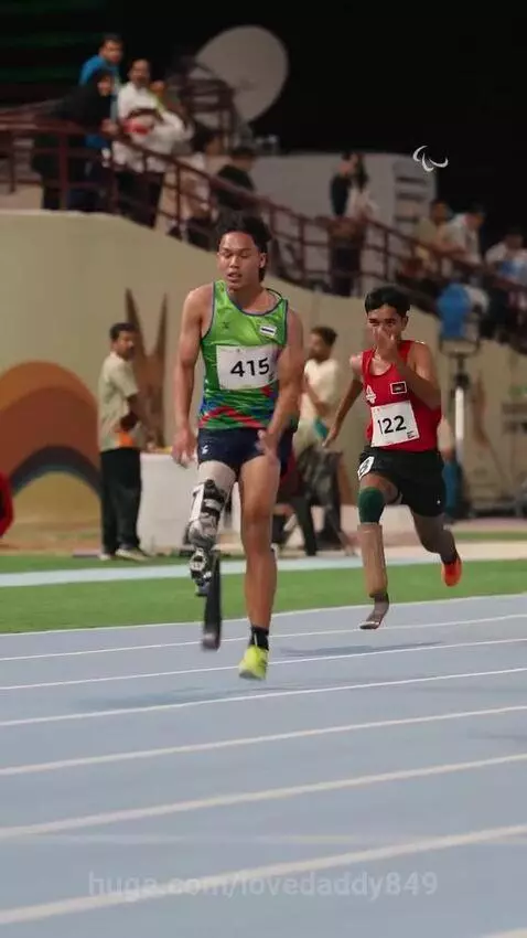 Athlete with a prosthetic leg sprinting on a blue track during a competition, wearing a green singlet.