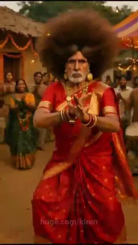 Men in colorful saris and funny wigs dancing with joy in a village celebration, with people clapping in the background.