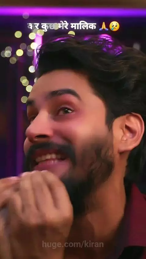 Man with beard crying, hands in prayer gesture, against blurred purple and yellow lights.