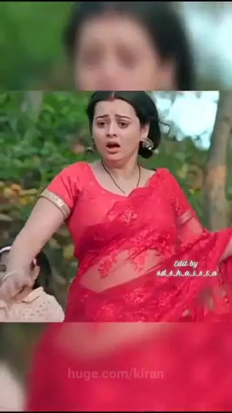 Woman in red saree and two crying girls beside a motionless man lying on the ground in a forest.