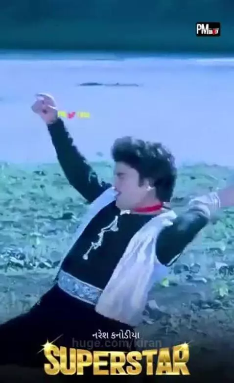 Man and woman in traditional Indian attire dancing energetically outdoors with a body of water and foliage.