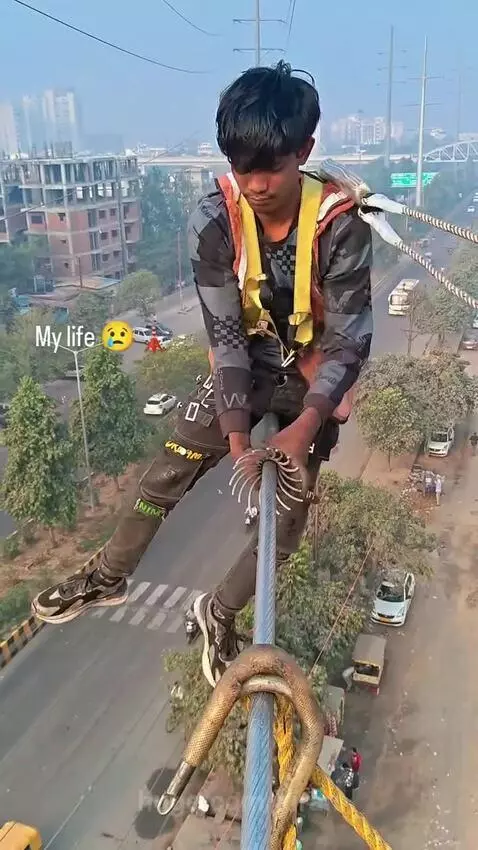 Young man in safety harness working on a thick cable high above a multi-lane highway with cars and buses below.