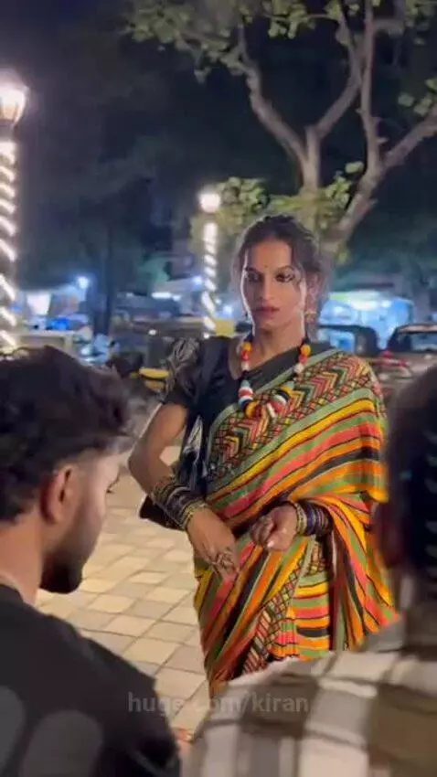 A transgender person in a colorful saree blesses a man who bows down to touch their feet.