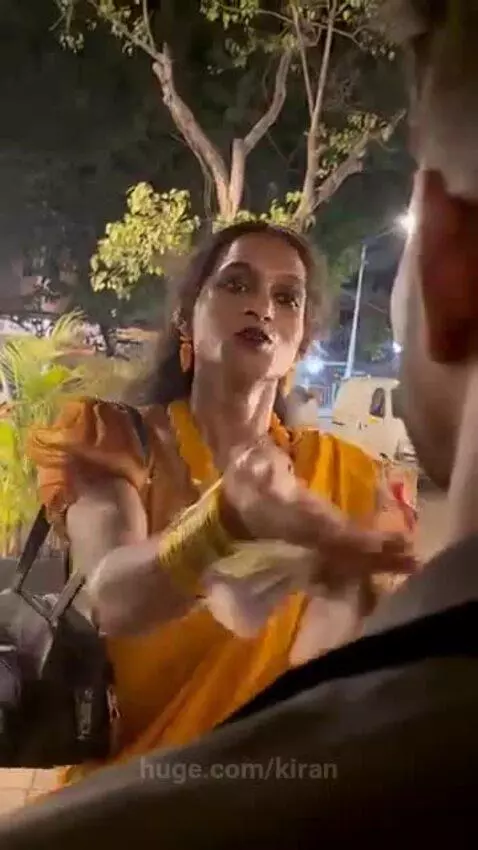 Transgender person in a yellow saree giving blessings to young men outdoors at night.