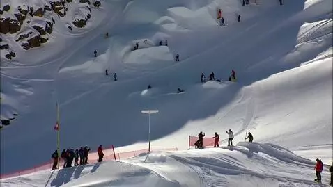 Aerial view of a busy snow park with snowboarders and skiers performing jumps on ramps and bumps.