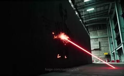 A red laser beam carves a glowing phoenix symbol onto a dark concrete wall, with sparks and smoke rising.