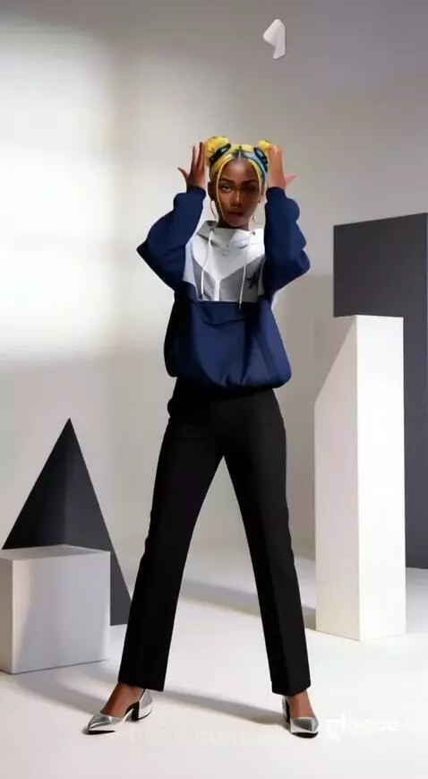 Woman with yellow and blue hair in buns, wearing a color-block hoodie and black pants, dancing energetically in a studio.