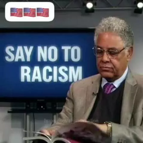 Man in suit jacket and purple tie speaks about racism, with 'Say No To Racism' on a screen behind him.
