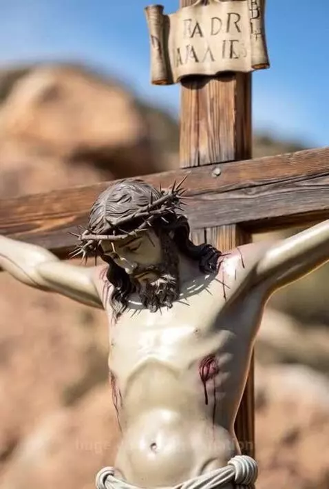 Statue of Jesus Christ on a wooden cross, wearing a crown of thorns, with golden light emanating from it.
