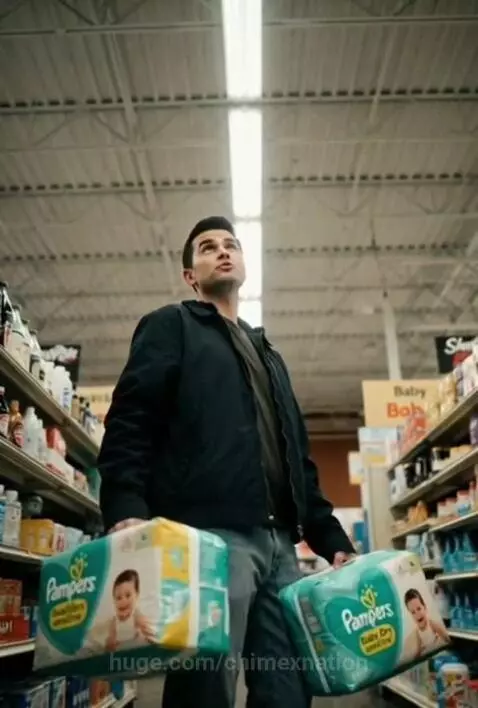 Man in supermarket diaper aisle looking pained, holding Pampers, offering life advice.