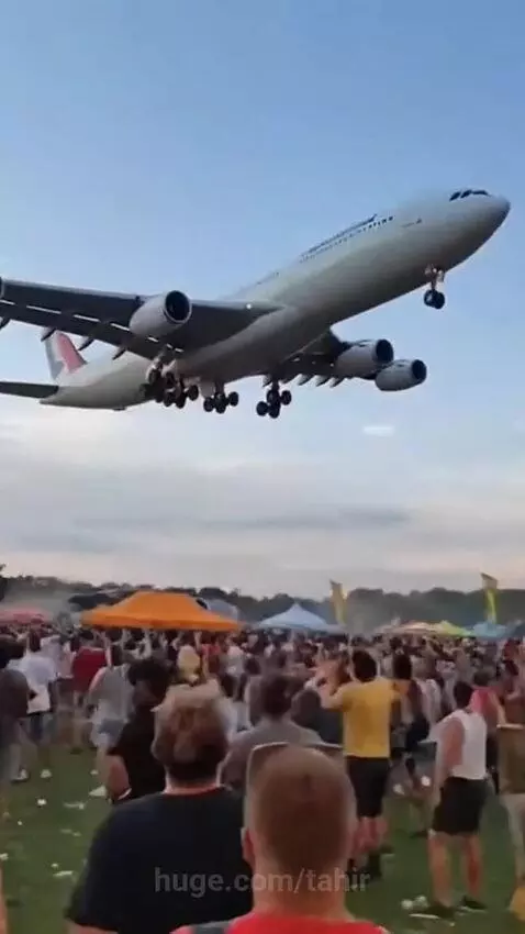 Airbus A340 flying extremely low over a large crowd at an outdoor music festival, crowd looking up in awe.