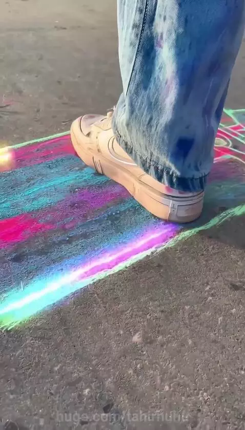 Person with pink hair drawing a skateboard with chalk, which then becomes real and glows as they ride it.