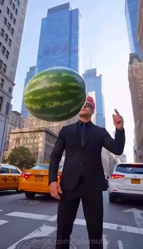 Man in a suit with pink hair stops a falling watermelon, which then slices into pieces around him.