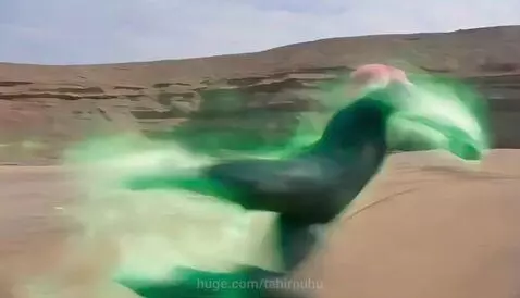 Two superhero-like characters fighting on a sandy beach, one with a green aura, the other in red armor, with energy effects.