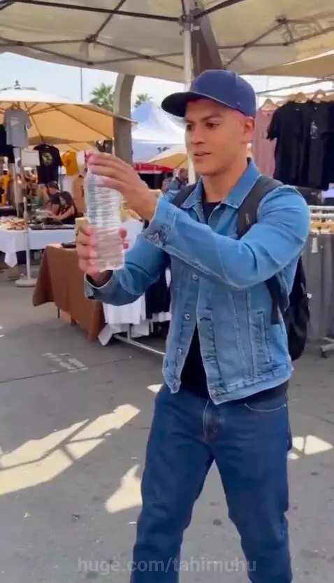 Man in denim jacket and baseball cap performing magic trick, turning water into floating crystals.
