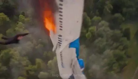 Superhero in a black suit flying and catching a man falling from a burning, exploding airplane.