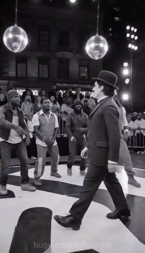 Street dancers perform a routine at night with disco balls, featuring a Charlie Chaplin impersonator with glowing effects.