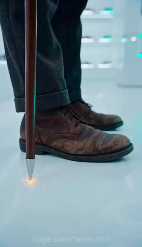 Man dressed as Charlie Chaplin walking up a glass wall with glowing, gravity-defying shoes.