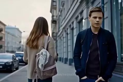 Young woman walking in a park, looking thoughtful, with a river and bridge in the background.