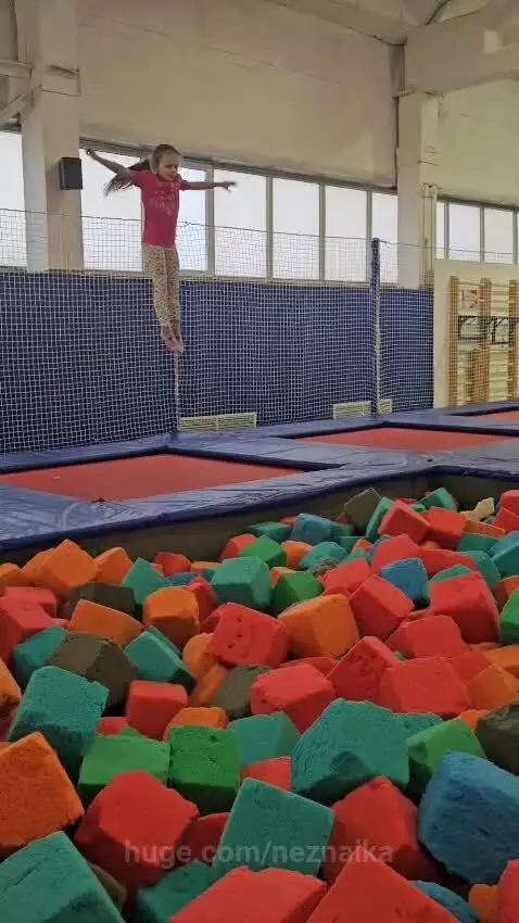 Young girl in pink t-shirt and leggings performing a front flip into a foam pit.