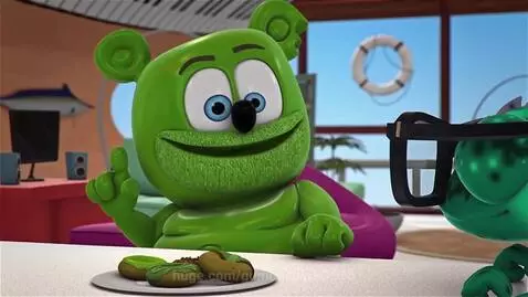 Green Gummy Bear character sitting at a table with donuts, smiling and pointing upwards, giving advice.