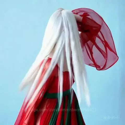 Woman with long, flowing white hair in a red and green dress spinning against a light blue background.