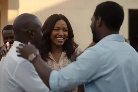Three adults, two men and one woman, smiling and embracing outdoors in golden sunlight.