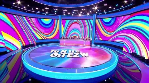 Modern Price Is Right game show set with a circular stage, glowing blue and pink rim, and a large curved LED screen displaying colorful patterns.