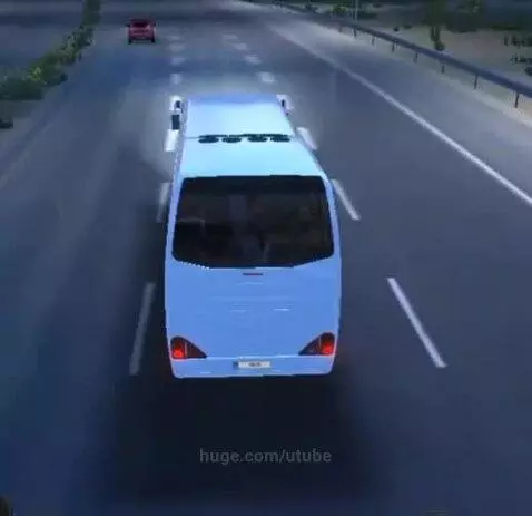 Light blue bus driving on a multi-lane highway at night, viewed from behind.
