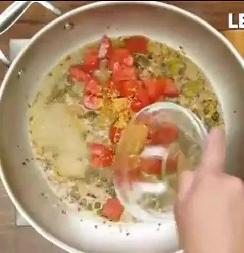 Close-up of a bowl of pasta with melted cheese, vibrant red tomatoes, and green capers.
