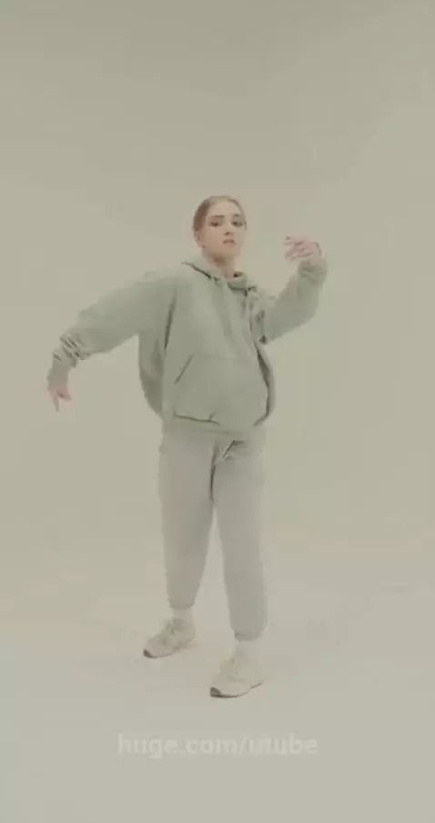 Young woman with light hair in a green hoodie performing a contemporary dance in a minimalist studio.