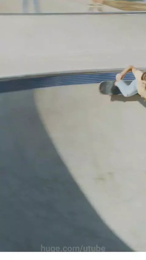 Young woman with long brown hair in yellow t-shirt and jeans skateboarding smoothly in a concrete park.