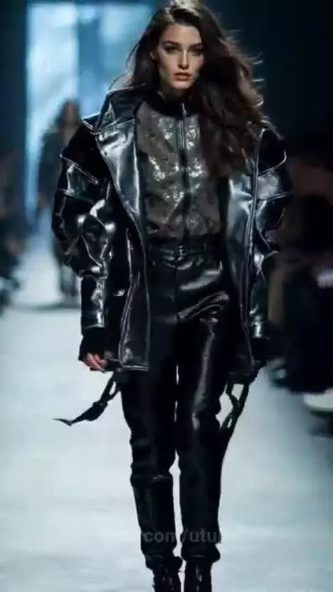 Model wearing an oversized black patent leather jacket and leather pants on a dimly lit runway.