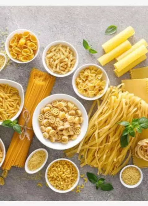Assortment of dry pasta types like spaghetti, penne, and fusilli, garnished with basil on a textured surface.