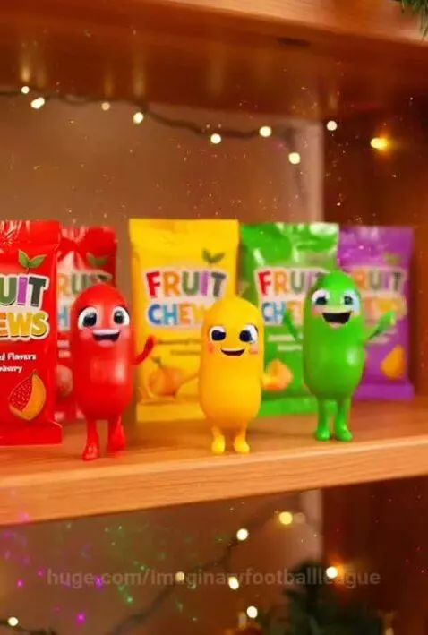Five colorful, anthropomorphic fruit chew characters dancing on a shelf with Christmas lights and ornaments.