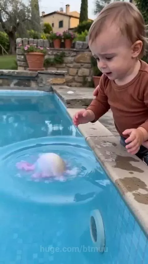 A baby's face lighting up with surprise and joy as colorful bath bomb foam swirls in the water, revealing a small toy.