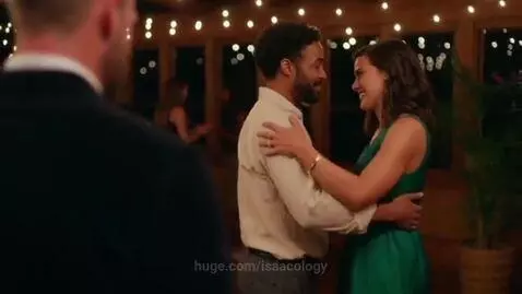 Couple dancing closely at an evening event, woman in green dress, man in light shirt, smiling under string lights.
