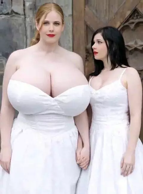 Two women in white dresses, one undergoing extreme breast enlargement and height growth, the other looking on in shock.