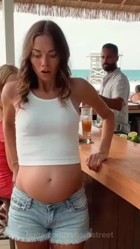Woman at beach bar with rapidly expanding stomach, looking surprised as her shorts button pops.