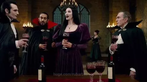 Vampires in costume gathered around a table with wine glasses in a dimly lit medieval castle.