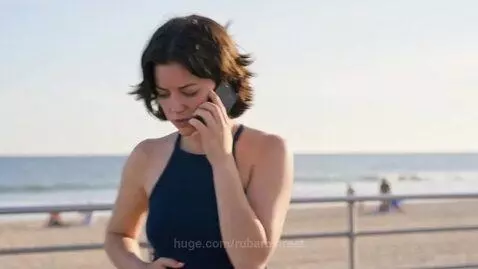 Woman on beach boardwalk looking distressed, talking on phone, with lifeguard approaching.