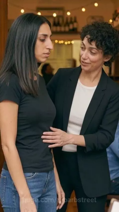 Woman in black blazer places hand on friend's stomach and asks 'Hungry?'